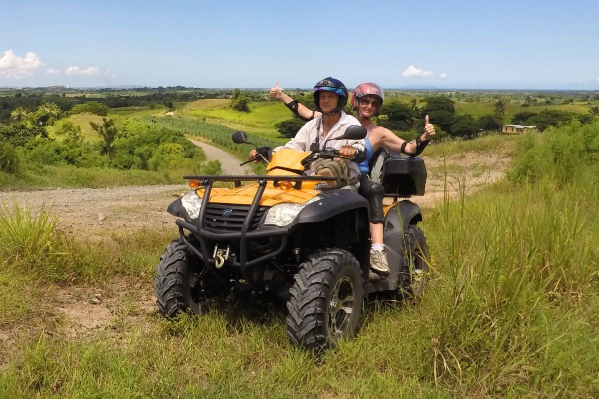 Couple on yellow ATV overlooking green rice paddies and mountain landscape on mainland Panay near Boracay, Philippines
