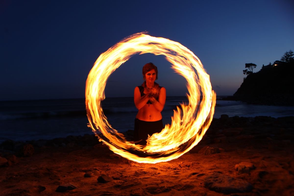 Fire dancer spinning flaming poi in perfect circle on beach at dusk in Boracay with ocean and twilight sky in background