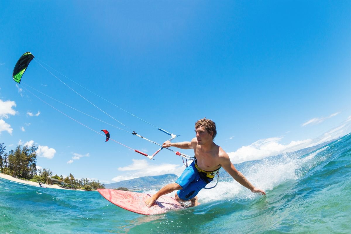 Kiteboarder riding waves at Bulabog Beach Boracay with colorful kite in clear blue sky and mountains in background
