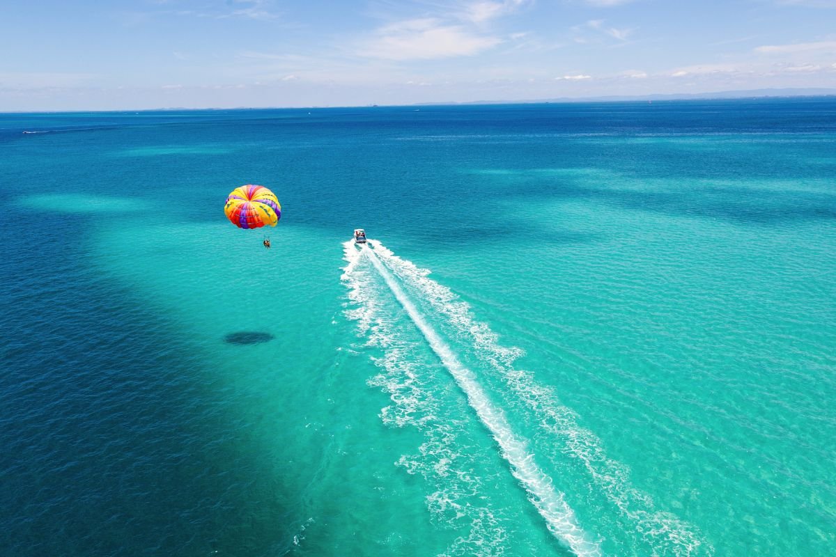 Aerial view of parasailing over crystal clear turquoise waters in Boracay with colorful rainbow parachute and speedboat trailing white wake

