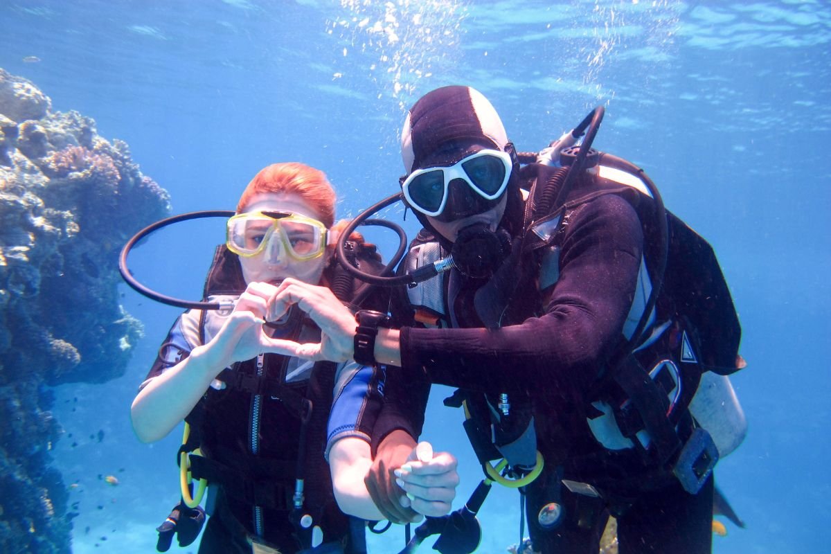 Couple scuba diving together making heart symbol with hands underwater near coral reef in Boracay, Philippines

