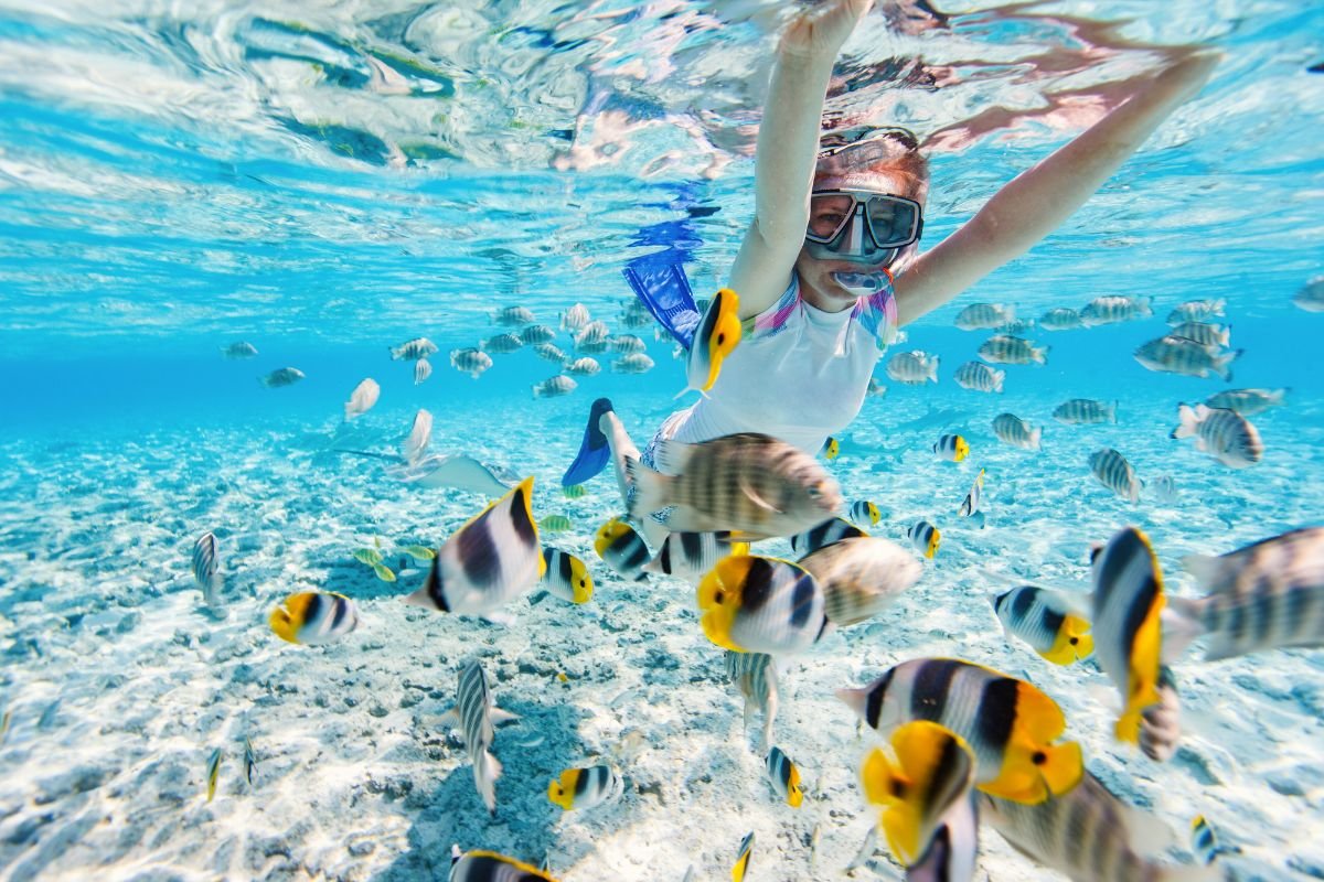 Woman snorkeling in crystal clear turquoise water surrounded by colorful tropical fish in Boracay, Philippines
